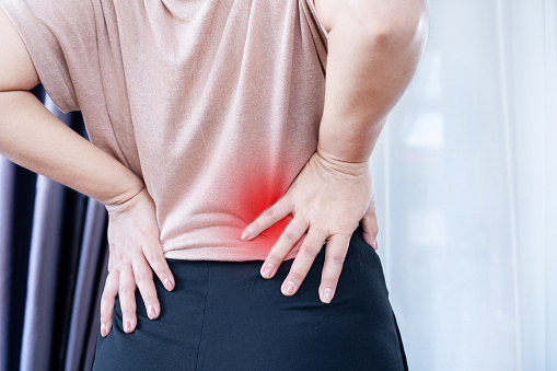 Closeup of a Woman with Lower Back Pain, Muscle Strain, and Spasms due to Prolonged Sitting and Poor Posture