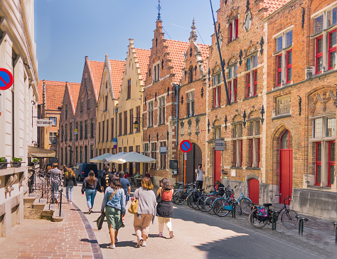 Bruges, Belgium-June 3, 2023- Pedestrians stroll down a narrow street in the old city of Bruges, past restaurants, shops, rows of parked bicycles and medieval architecture.