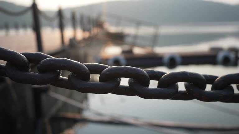 Close-up tracking shot of iron thick chain fence on jetty on lake stretched for safety on wooden pier, on background of sunlight during sunset.
