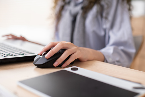 Details of woman's hands working using a mouse on a desktop