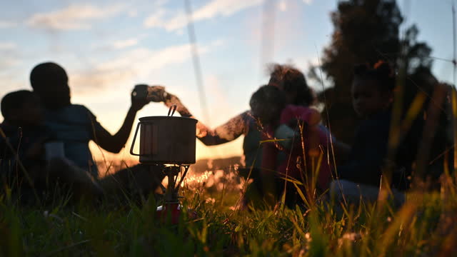 African family with camping gas stove with steam enjoying a hot drink picnic at sunset