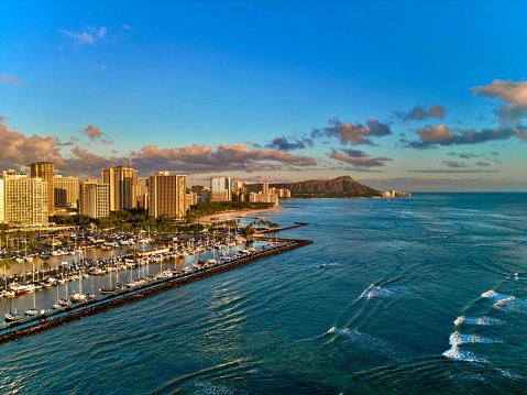 Aerial view of a vibrant cityscape of Diamond Head Sunset, Waikiki, Hawai'i featuring numerous boats cruising along the shoreline