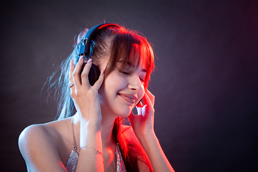 Portrait of attractive young white woman with wireless headphones in studio against a black background