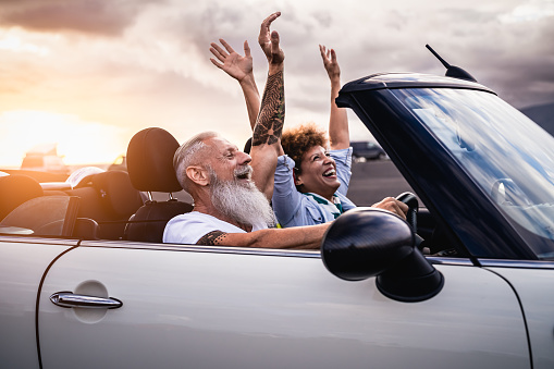 Happy senior couple having fun driving on new convertible car - Mature people enjoying time together during road trip tour vacation - Travel people lifestyle concept