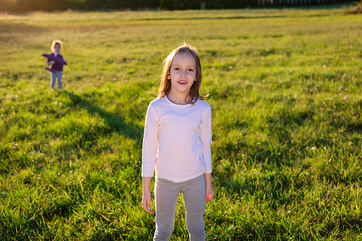 Girl standing on the meadow during spring day and looking at camera. There is child in the background.