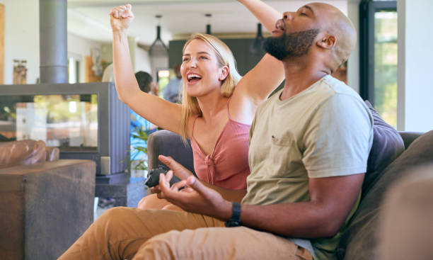 istock Couple On Sofa At Home Together Playing Computer Game With Woman Winning 1500615969