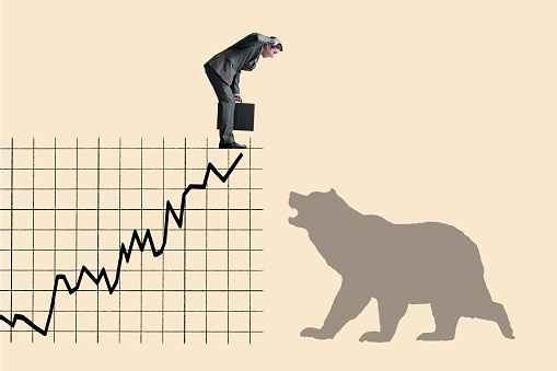 A man looks down at the silhouette of a bear as he stands at the top of a chart showing a stock market rally.