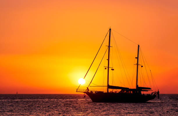 silueta de velero con velas hacia abajo contra el sol al atardecer, resplandor del sol en las aguas del mar. paisaje marino romántico, cuerdas de vela de toque de sol. - headsail fotografías e imágenes de stock