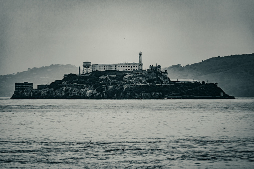 Black and white photograph of the alcatraz jail as seen from pier 39 of the fisherman's wharf in San Francisco bay, a city in the state of California in USA. Concept boats.