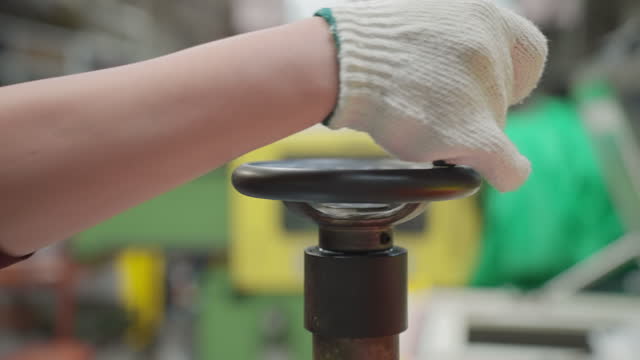 A female scientist's hand reaches for the manufacturing production machine's valve in an attempt to open it.