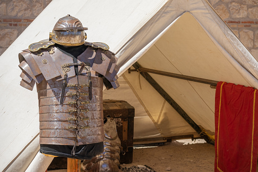 horizontal view in foreground of an exhibitor with armor and imperial helmet of a soldier from ancient roman empire in front of a military tent, lorica segmentata and galea of a roman legionary soldier