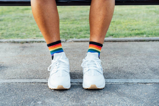 acerque las piernas de las personas lgbt con calcetines de arco iris y zapatos blancos en el suelo de concreto. soledad, tristeza por la discriminación homosexual. luchar por la igualdad, la libertad, los derechos humanos. mes del orgullo. - emitir fotografías e imágenes de stock