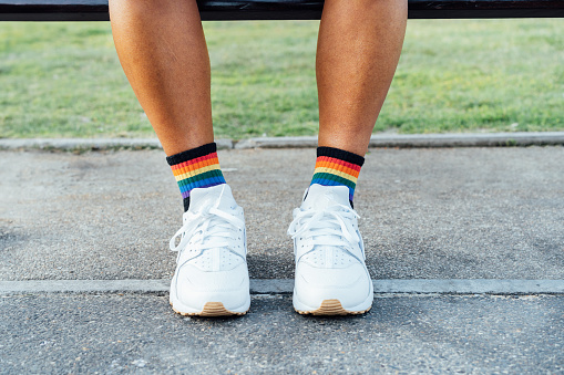 Close up LGBT persons legs wearing rainbow socks and white shoes on concrete ground. Loneliness, sadness for homosexual discrimination. Fight for equality, freedom, human rights. Pride month