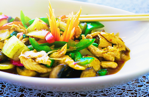 Brightly lit bowl of healthy Thai food, topped by a beautifully carved decorative carrot.