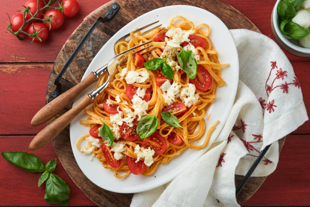 salat-caprese oder pasta-spaghetti gebrochen mit basilikum und mozzarella ala caprese auf einem weißen teller auf rotem rustikalem holzhintergrund. traditionelle italienische küche. italienisches food-konzept.  draufsicht. - caprese salad antipasto wine mozzarella stock-fotos und bilder