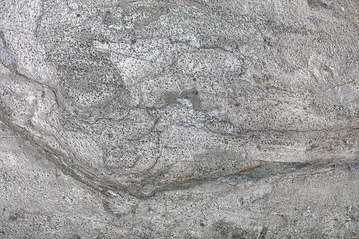 The surface of volcanic lava with spots and streaks after cooling and turning it into stone. Natural gray texture and background.