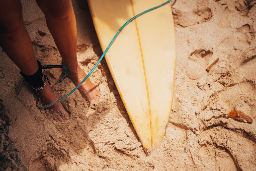 Female surfer legs with yellow surfboard on the beach next to her.