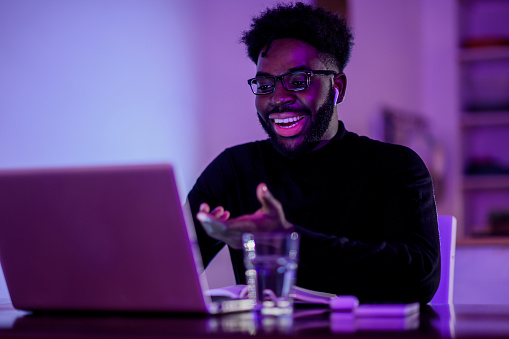 A happy interracial remote worker is having a video call with a client late at night from home. A friendly freelancer is sitting at home at night and having a conference call with a client or team.