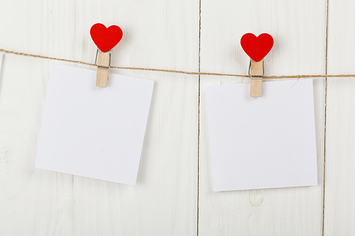 white pieces of paper on clothespins with a heart on a wooden background close-up