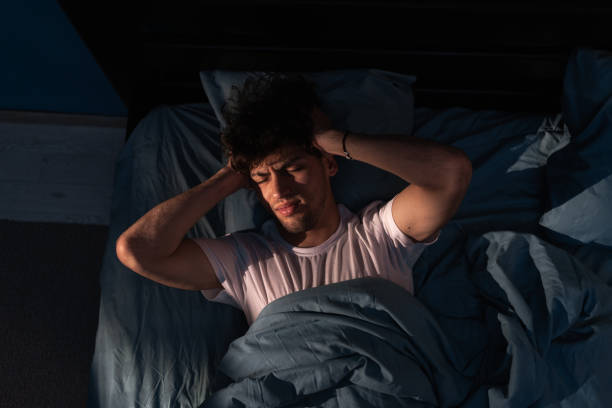 istock Muslim young man suffering from headache while lying in bed at night. Insomnia. Top view 1500658312