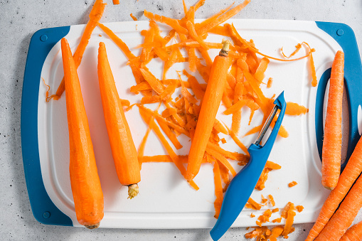 Peeled carrots close-up on a white cutting board on a kitchen table, flat lay