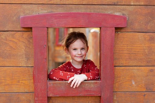 Portrait of a cute little girl in front of a wooden house