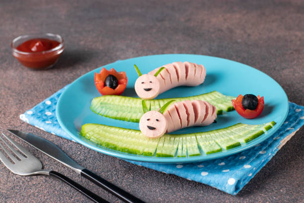 Breakfast or lunch for a child - a caterpillar of sausages with cucumber and cherry tomatoes on blue plate stock photo