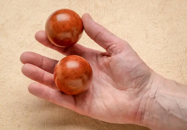male hand holding a pair of wooden Chinese medicine balls against textured paper