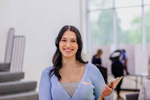 The cheerful young adult female volunteer poses for a portrait at the polling place.