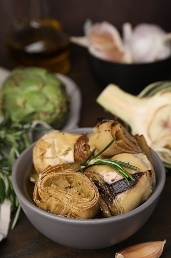 Bowl with delicious artichokes pickled in olive oil on wooden table, closeup
