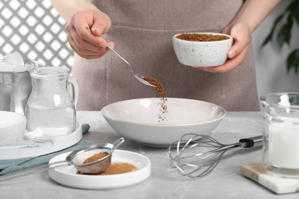 istock Making dalgona coffee. Woman pouring instant granules into bowl at light gray table, closeup 1500681192