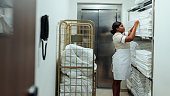 African-American hotel maid preparing clean sheets in laundry