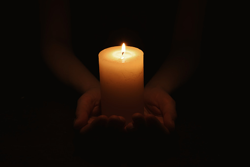 Woman holding burning candle in hands on black background, closeup