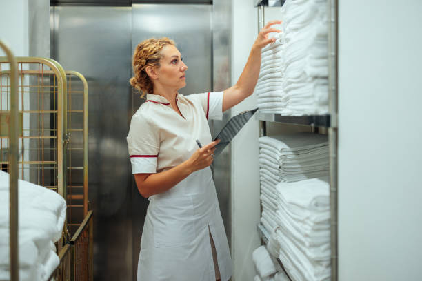 istock Caucasian young uniformed maid counting clean bed sheets in hotel laundry 1500684657