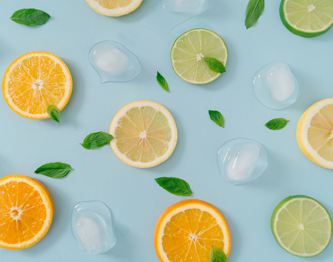 Creative summer background composition with orange, lemon and lime slices, green mint leaves and ice cubes. Minimal top down lemonade drink concept. Citrus fruit aesthetic. Flat lay background.