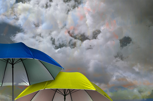 two open blue and yellow umbrellas against a dramatic white cloud background with a rainbow effect