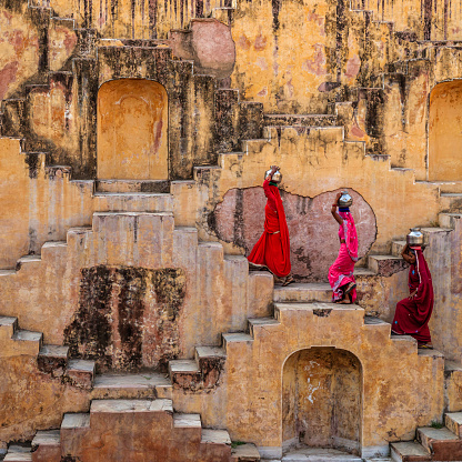 Indian women carrying water from stepwell near Jaipur, Rajasthan, India. Women and children often walk long distances to bring back jugs of water that they carry on their head. \nStepwells are wells in which the water may be reached by descending a set of steps.