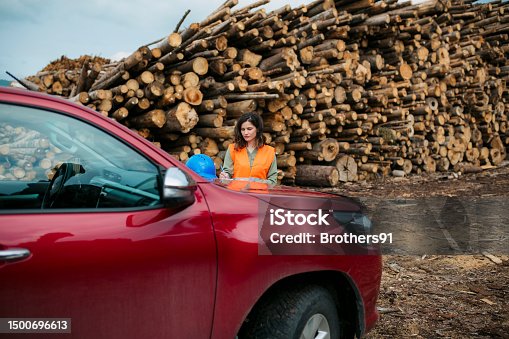 istock Woman supervisor in front of a vehicle in timber yard with wood pile in background 1500696613