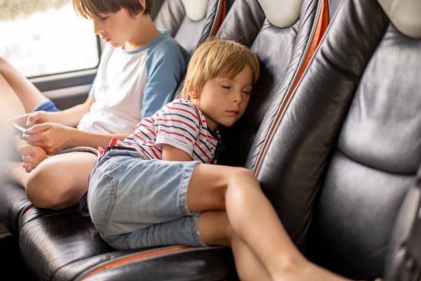 istock Child, cute blond boy, sleeping in the bus on a way back from holiday, older brother playing on the phone 1500700377