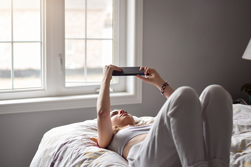 Young teenage girl lying on her back on top of bed using wireless tablet