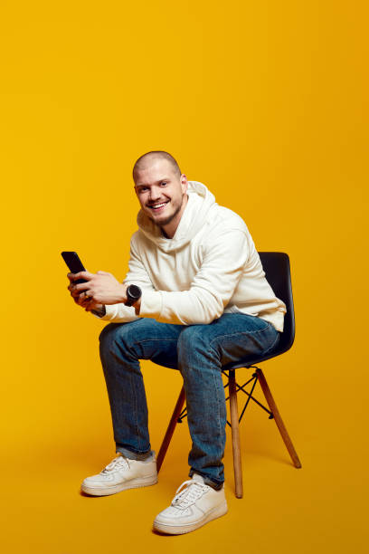 istock Attractive bearded man using smartphone while sitting on chair isolated on yellow background 1500708086
