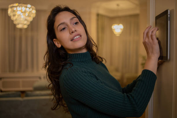 istock Young woman adjusts the temperature at home with a device on the wall 1500714372