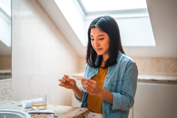 Excited Asian Female Performing Pregnancy Test At Home Excited Asian female performing pregnancy test in a domestic bathroom. Dipping test into urine to read results. human fertility stock pictures, royalty-free photos & images