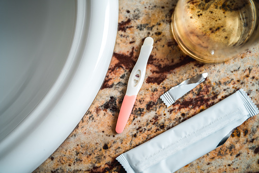 Close up on a pregnancy test on a bathroom sink and a urine sample in a glass.