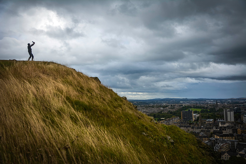 Silhouette of a man holding his camera high on the edge of a cliff.