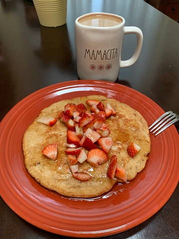 Fresh Strawberries & Maple Syrup Over a Homemade Pancake in Front of a Hot Cup of Coffee with the Words 