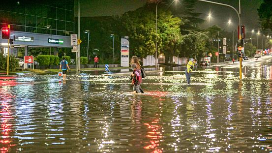 Auckland, New Zealand - January 27, 2023: Flooding after a record breaking heavy rain caused chaos in many suburbs in Auckland. The image was taken at the intersection of Greenlane, showing 2 people crossing the intersection guided by a police officer in the flooded water up to their knees.