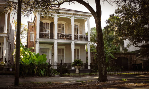 A beautiful historic home with a balcony and tall pillars in New Orleans,  Louisiana with tropical plants in the front yard