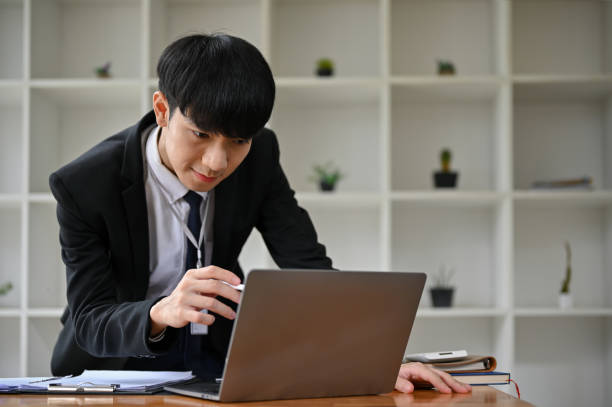 istock A determined Asian businessman is looking down and pointing pen at his laptop screen. 1500742905