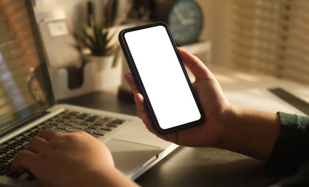 istock Close up view of woman hand holding mobile phone and using laptop computer. 1500743471